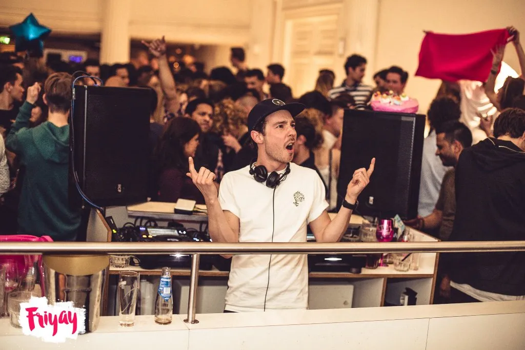 DJ in een volle zaal, met gasten rond de DJ-booth