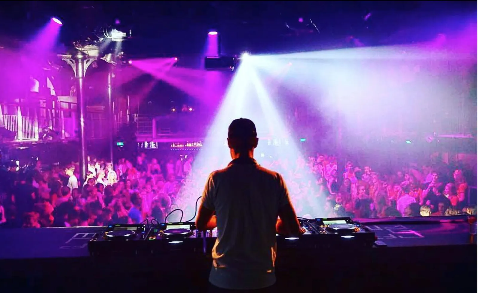 Silhouet van een DJ voor een zaal vol paarse lichtbundels